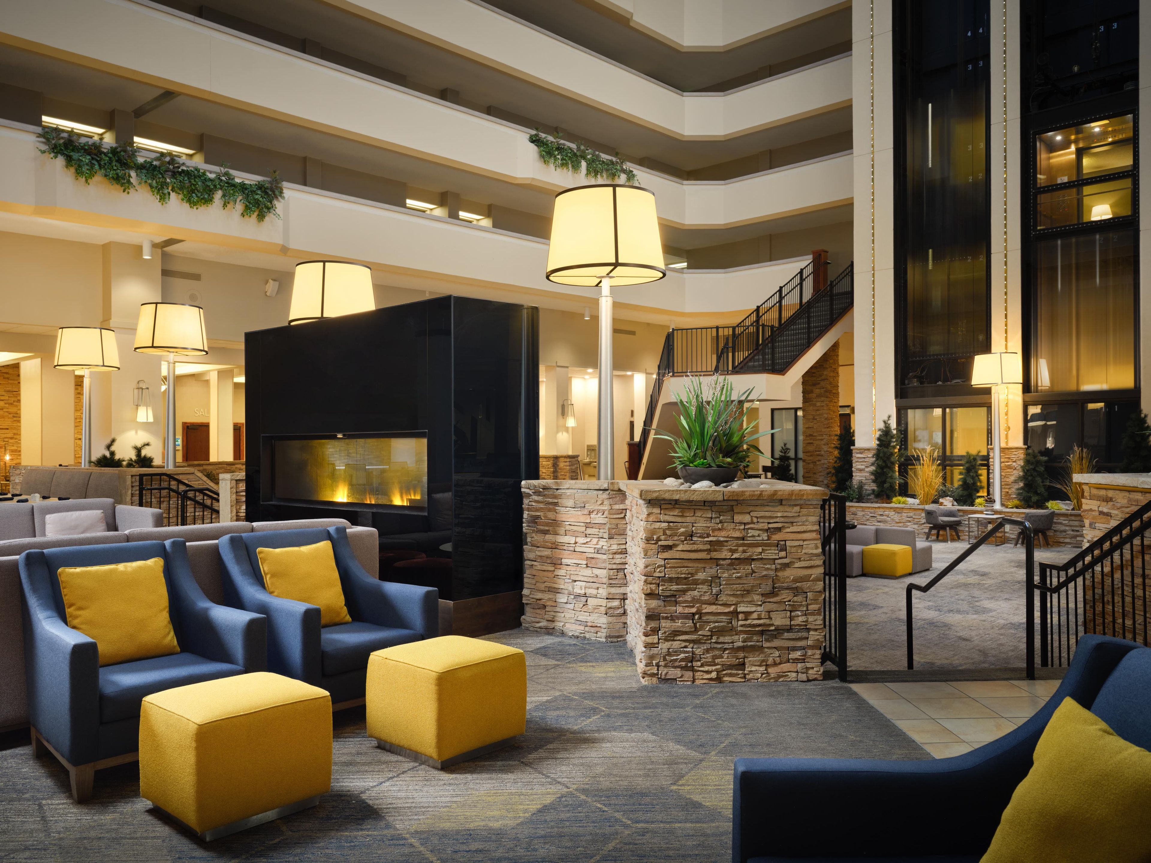 A spacious lobby with a fireplace, comfortable seating, a staircase, and a view of the upper floors.