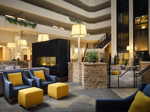 A spacious lobby with a fireplace, comfortable seating, a staircase, and a view of the upper floors.