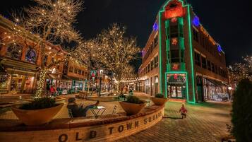 Un edificio histórico con una torre de reloj, rodeado de árboles decorados con luces, y una plaza pavimentada con bancos.