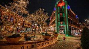 Un edificio histórico con una torre de reloj, rodeado de árboles decorados con luces, y una plaza pavimentada con bancos.