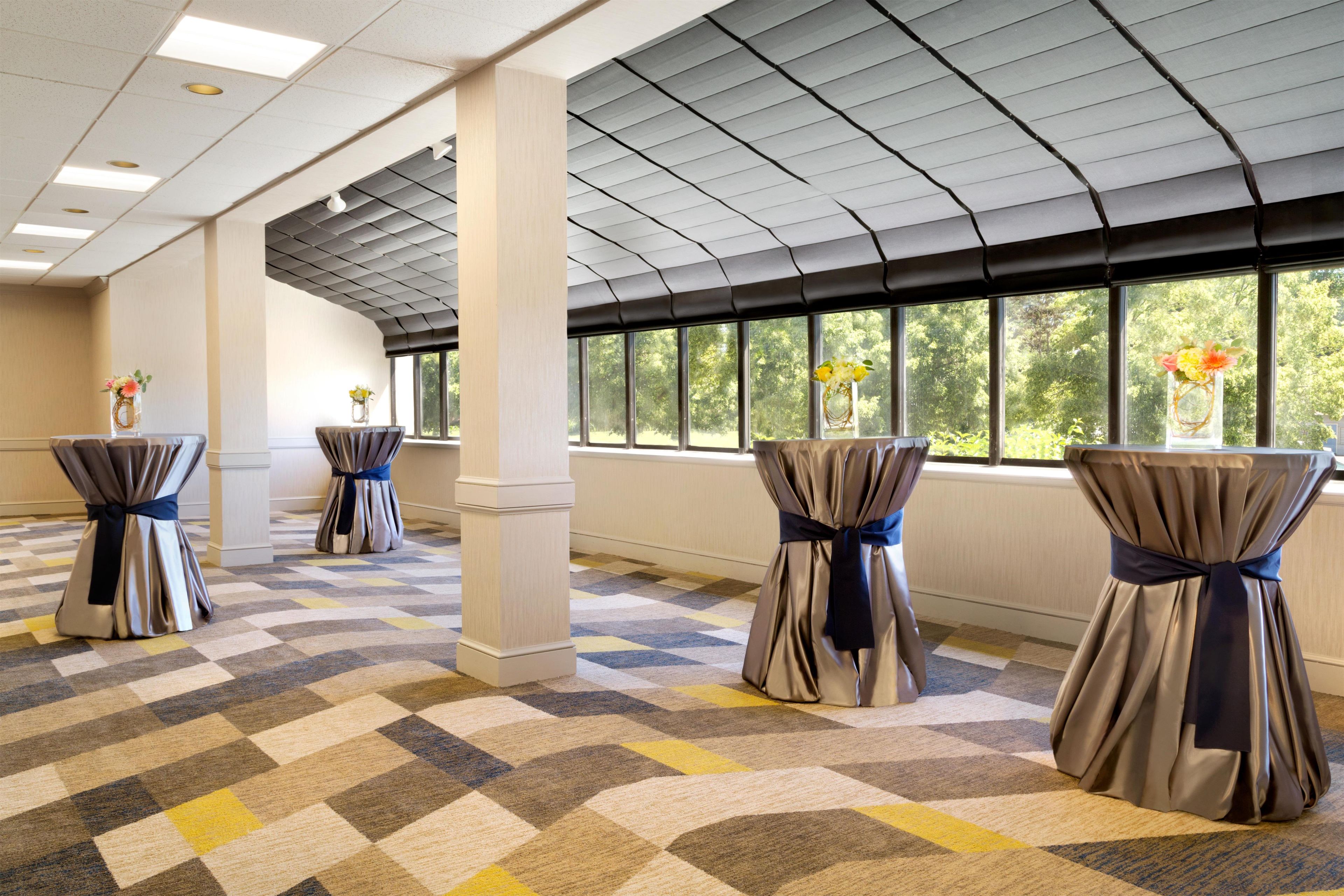 A hotel room with a checkered carpet, large windows, and curtains tied with ribbons.