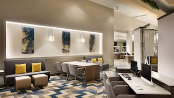 Um hall de hotel moderno com área de estar, balcão de recepção e uma grande parede com arte abstrata.