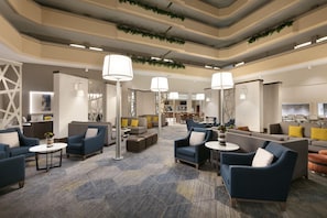 Un vestíbulo amplio con varias zonas de estar, incluyendo sofás y sillones, y un mostrador de recepción.