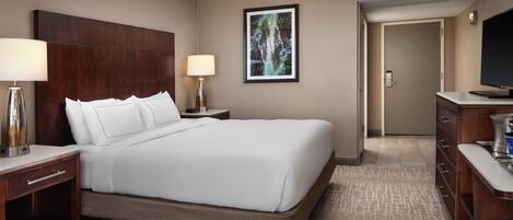 A hotel room with a large bed, two bedside tables with lamps, a flat-screen TV, a wooden dresser, and a framed picture on the wall.