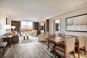 A hotel room with a large window, a dining area, a sofa, and a television. - Hilton Fort Collins (Fort Collins)