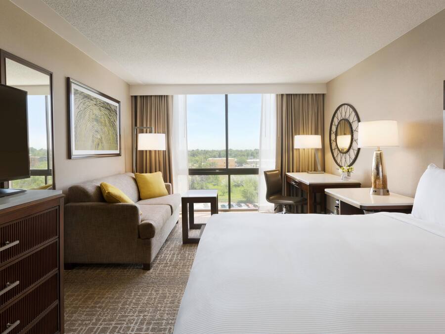 A hotel room with a bed, a desk, a chair, a television, and a large window.