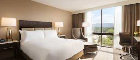 A hotel room with a large bed, two bedside lamps, a chair, a desk, and a view of the outdoors.