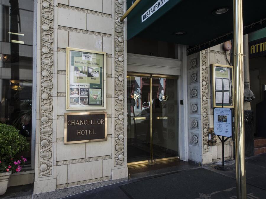 The exterior of the Chancellor Hotel with a glass entrance, a signboard, and an ATM on the right.