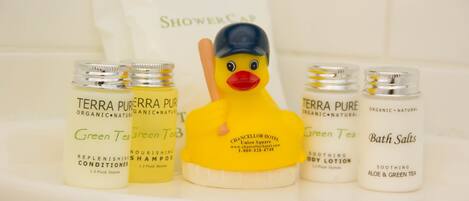 Un estante en el baño con champú, acondicionador y sales de baño Terra Pure, un patito de goma y un gorro de ducha.