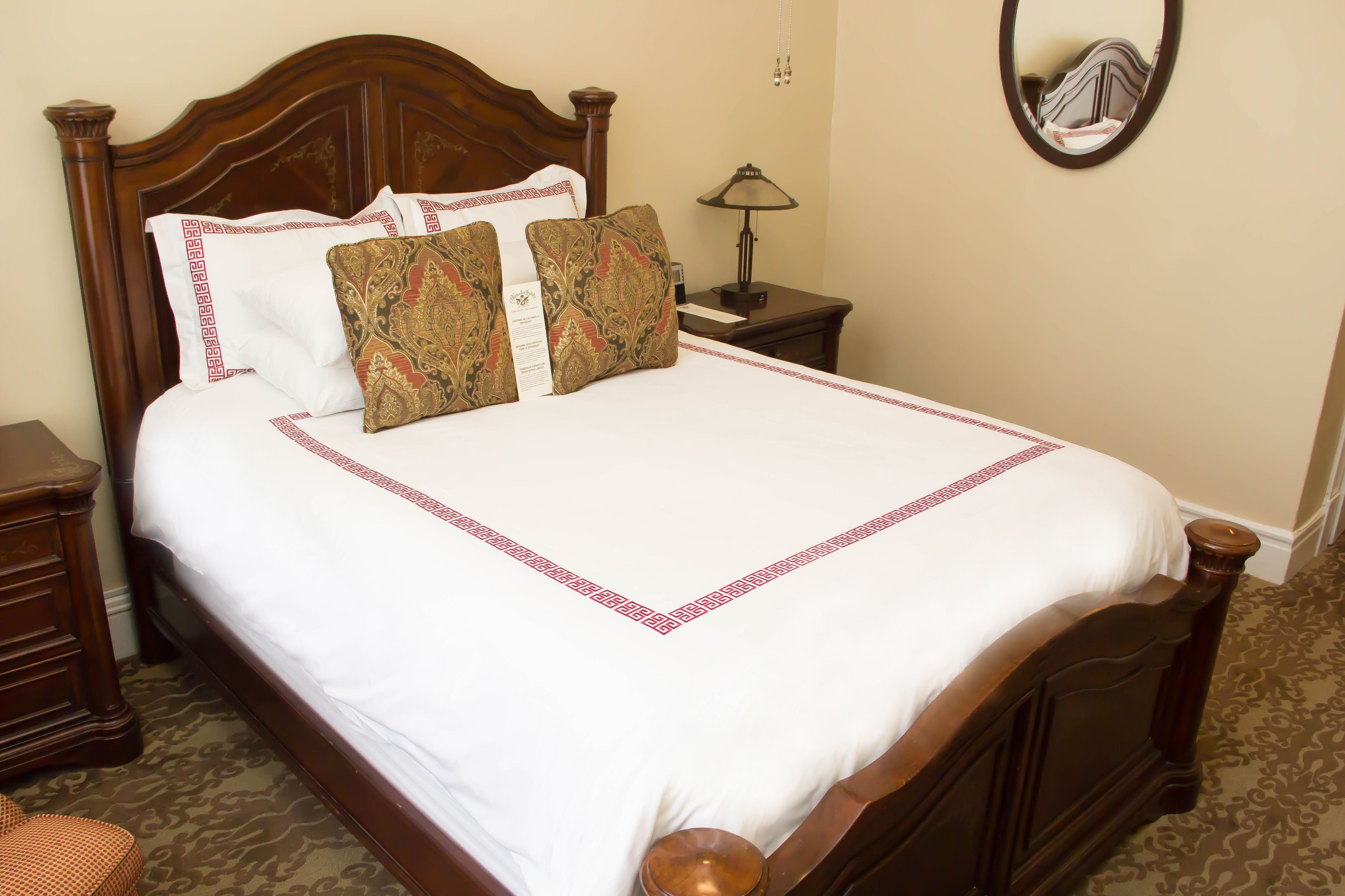 A neatly made bed with a wooden headboard, a bedside table with a lamp, and a mirror on the wall.