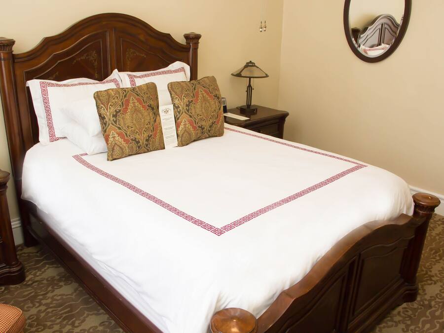A neatly made bed with a wooden headboard, a bedside table with a lamp, and a mirror on the wall.