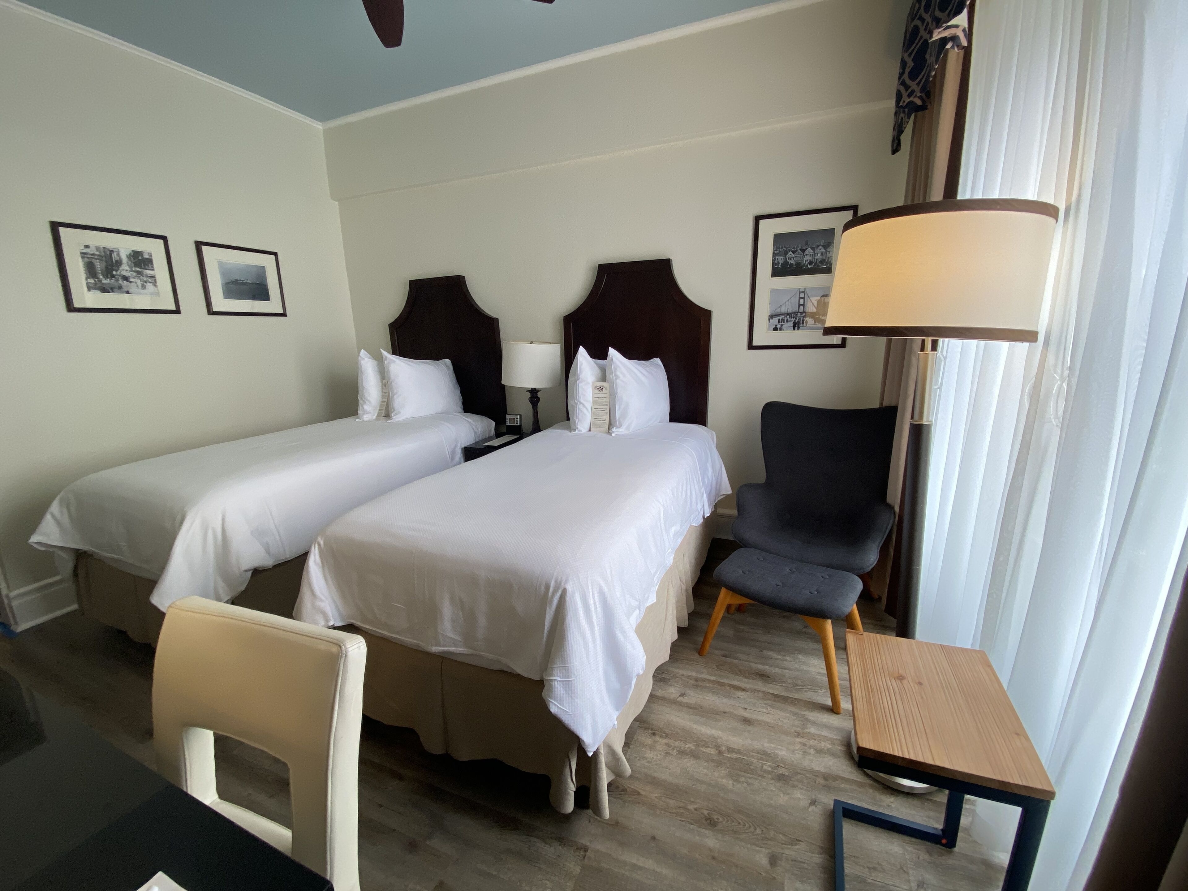 A hotel room with two beds, a desk, a chair, and a lamp.