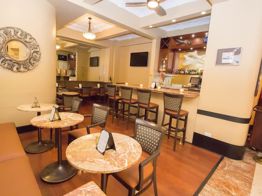 A restaurant with round tables, cushioned seating, a bar area, and a ceiling fan.