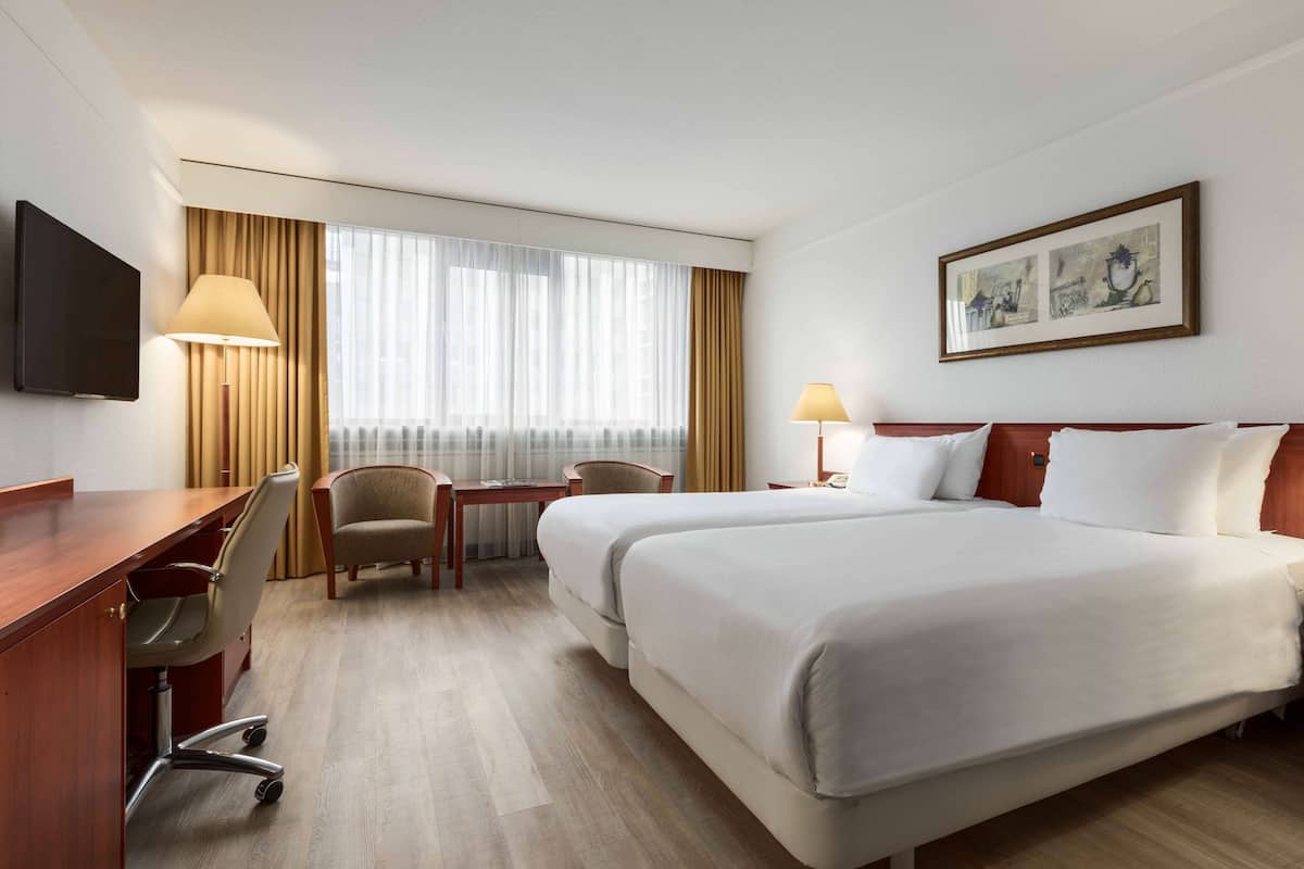 A hotel room with two beds, a desk with a chair, a television, and a window with curtains.