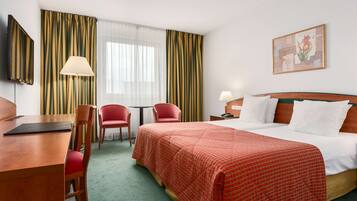 Een hotelkamer met een bed, twee stoelen, een bureau, een lamp en een schilderij aan de muur.