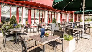 An outdoor cafe with tables and chairs, potted plants, and umbrellas. - NH Maastricht (Maastricht)