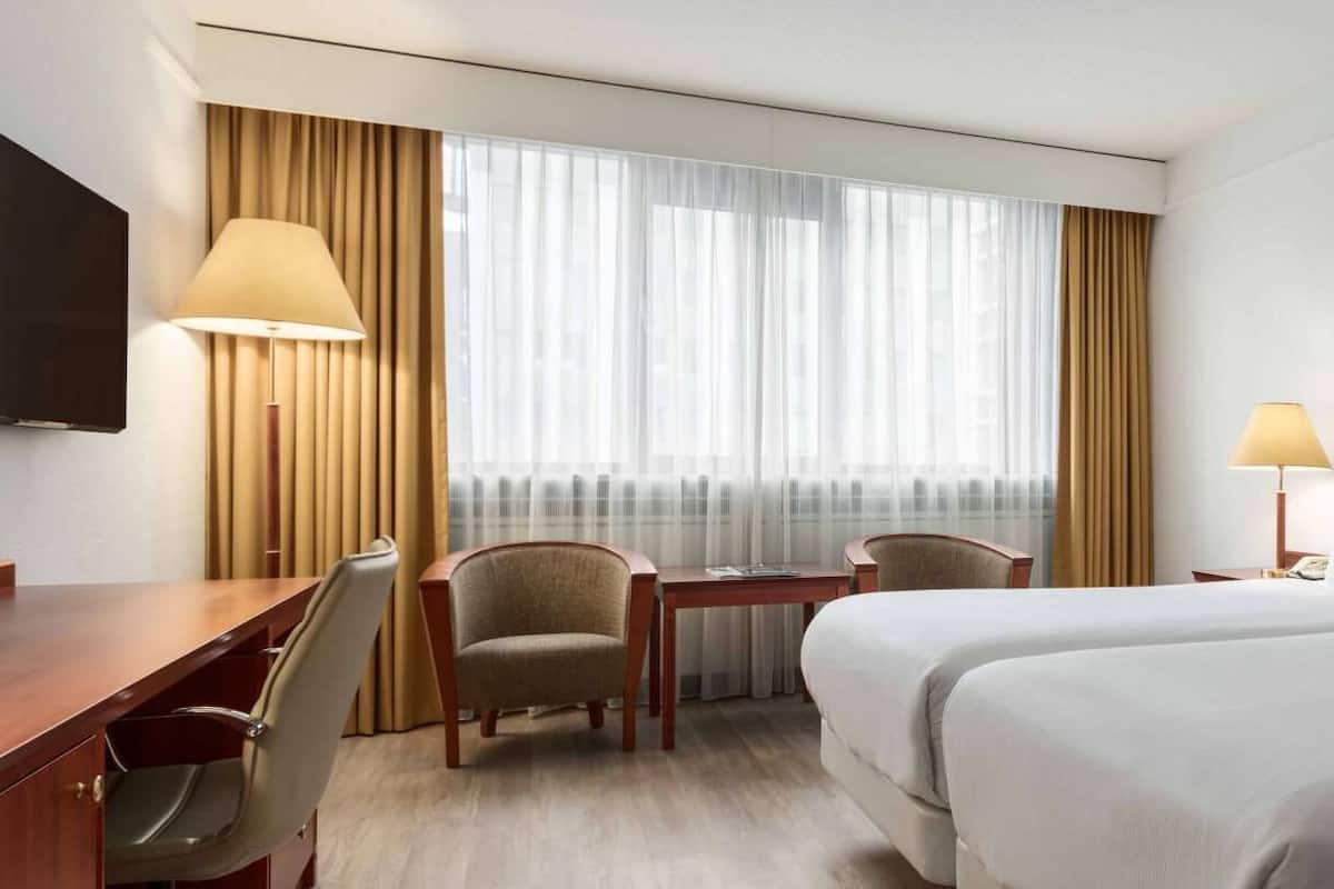 A hotel room with two beds, a desk, a chair, a television, and a window with curtains.
