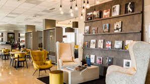 A modern lobby with seating areas, a coffee table, and a wall displaying various books and artwork. - NH Maastricht (Maastricht)