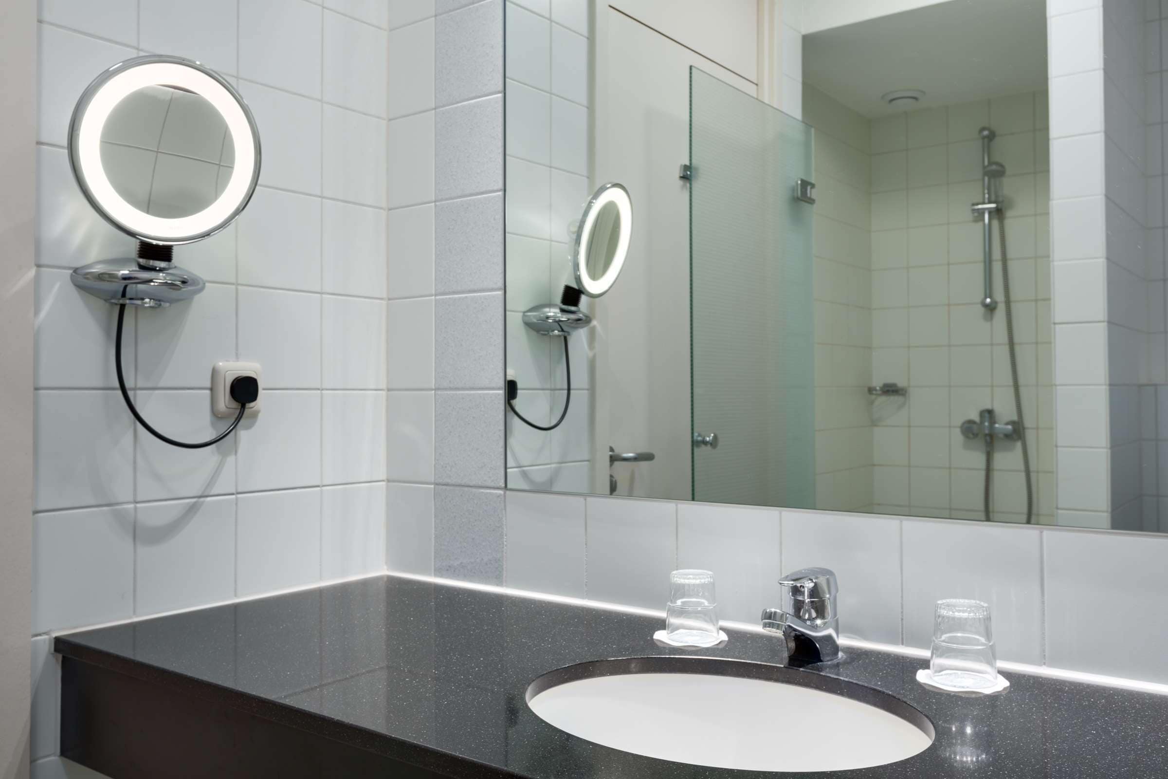 Un bagno moderno con uno specchio rotondo, due luci ad anello, un lavandino e una doccia.