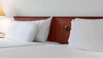 A hotel room with a wooden headboard, white bedding, and a bedside lamp.