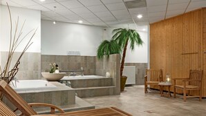 A spa area with a large bathtub, a wooden bench, and a potted palm tree. - NH Maastricht (Maastricht)