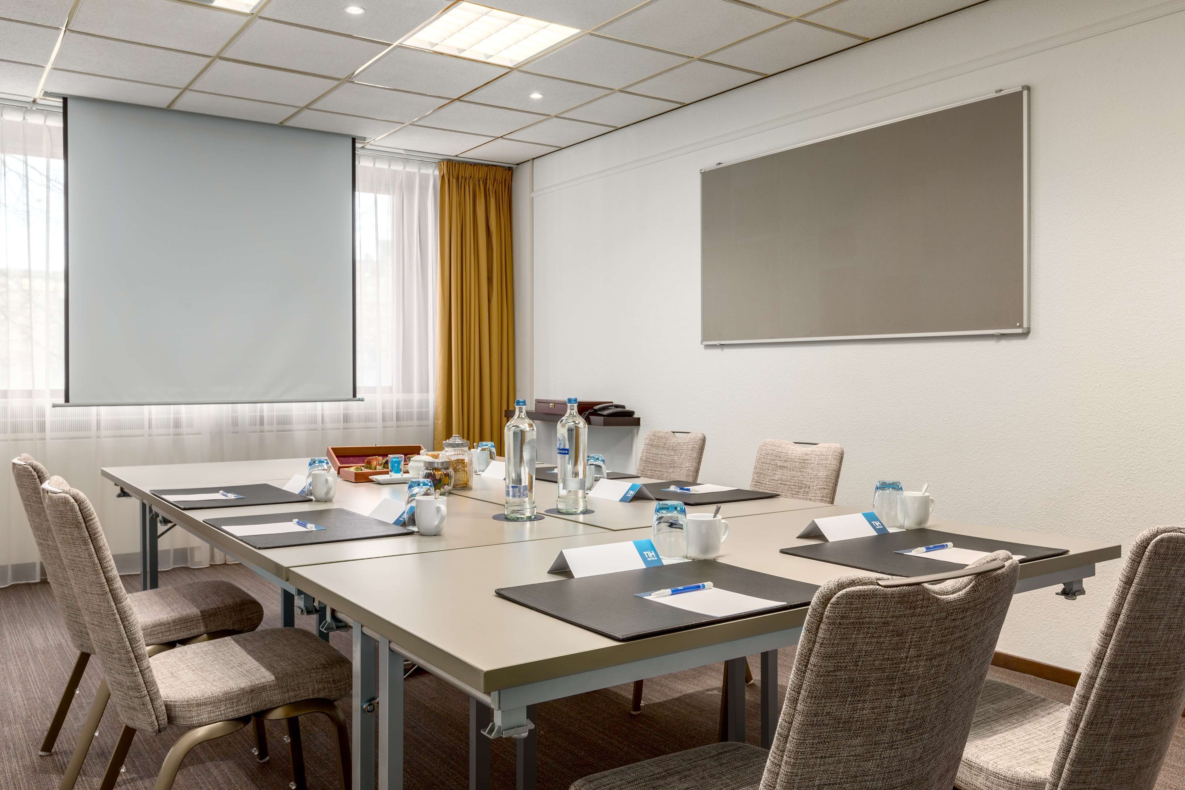 Una sala de conferencias con una mesa larga, sillas, una pantalla de proyector y una pizarra.