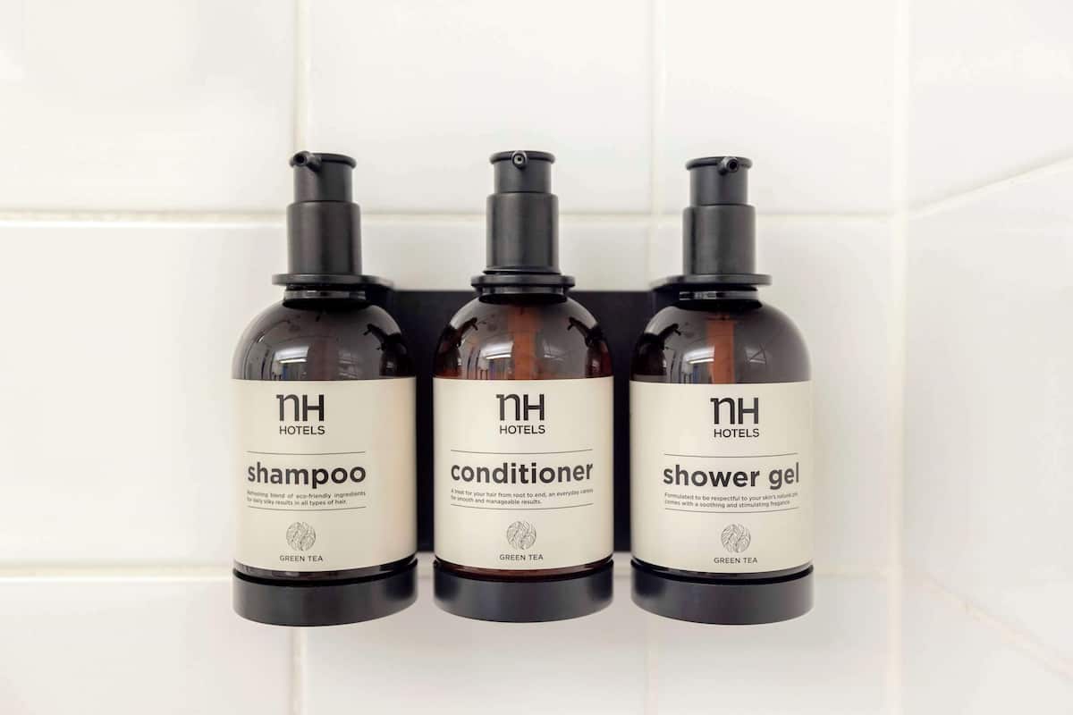 Three bottles of hotel amenities: shampoo, conditioner, and shower gel, labeled with 'NH Hotels' and 'GREEN TEA'.