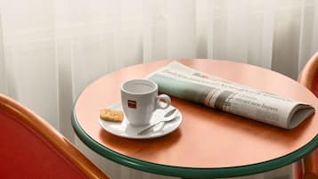 Una mesa redonda de vidrio con una taza blanca y una galleta en un plato, un periódico, y una silla roja.