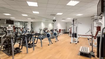 Een sportschool met diverse fitnessapparaten, waaronder loopbanden, hometrainers en krachttoestellen.