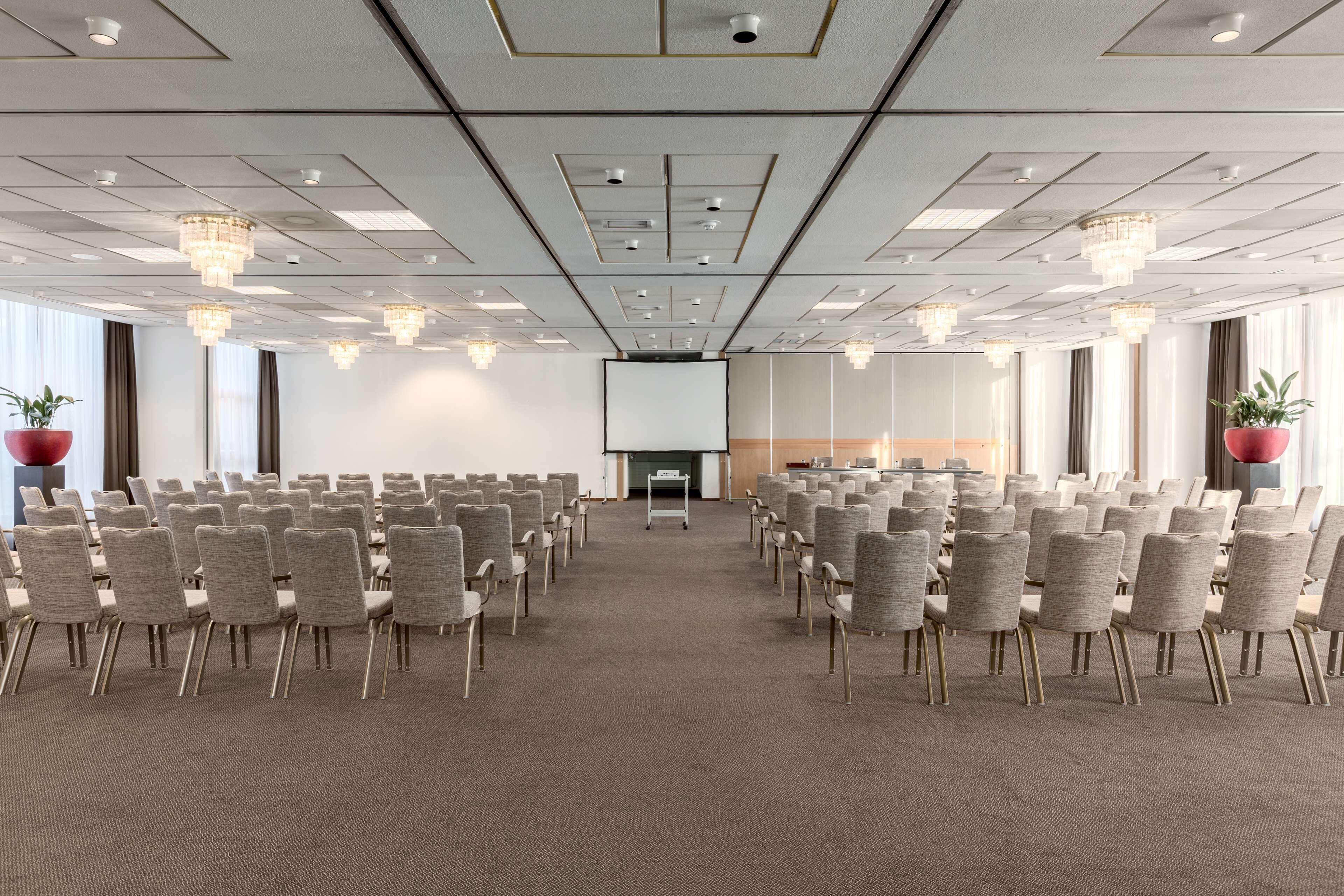 A conference room with rows of chairs, a projector screen, and a stage area.