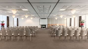 A conference room with rows of chairs, a projector screen, and a stage area.
