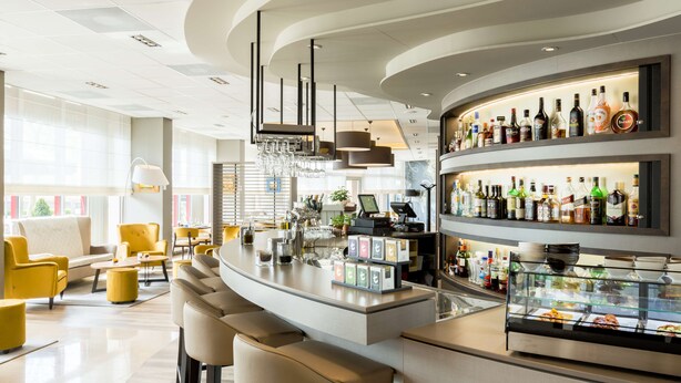 A modern bar area with a curved counter, bar stools, and a variety of liquor bottles. - NH Maastricht (Maastricht)