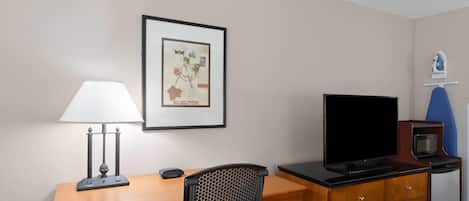 Habitación de hotel con un escritorio de madera, una silla de oficina negra, un televisor de pantalla plana, un microondas y una obra de arte enmarcada en la pared.