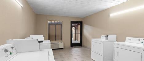 A laundry room with four white washers and dryers, a tiled floor, and a sloped ceiling with fluorescent lighting.