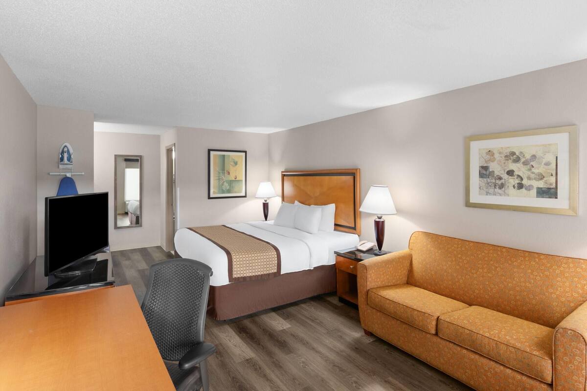 A hotel room with a bed, a desk with a television, a sofa, and two lamps.