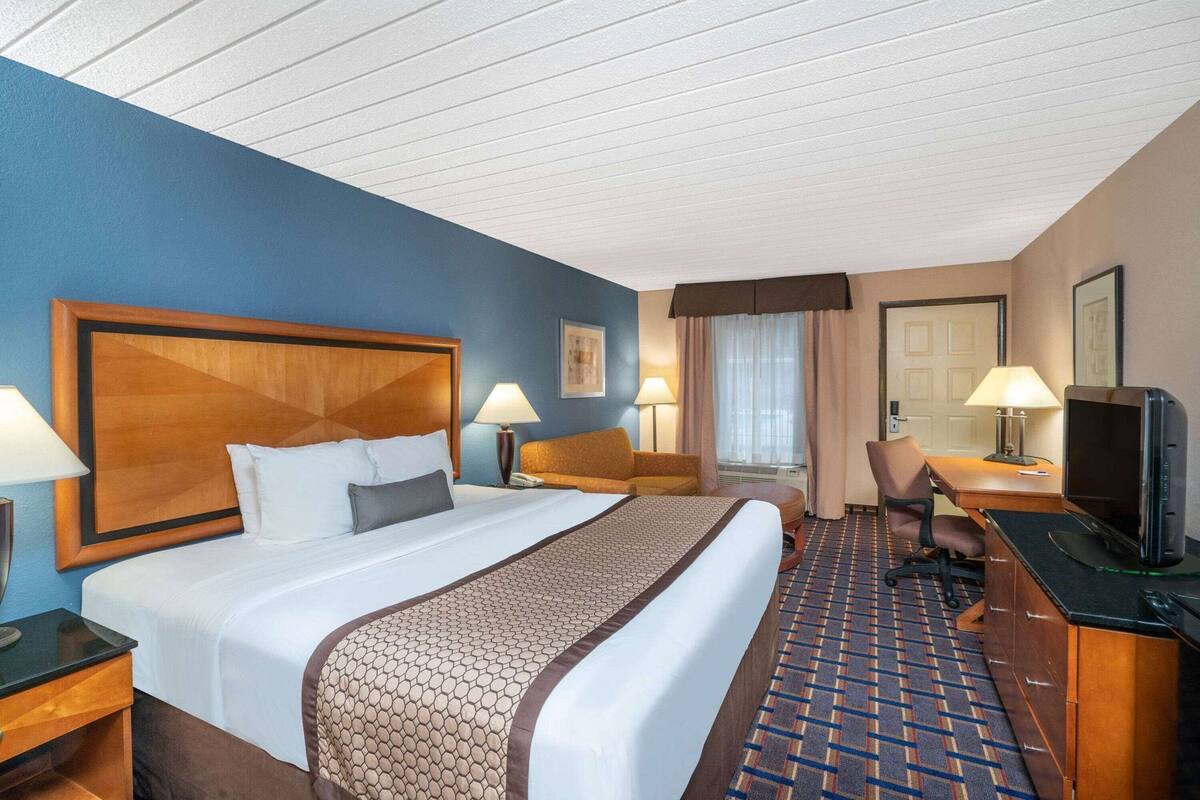 A hotel room with a large bed, a desk with a computer, a chair, a lamp, and a television.