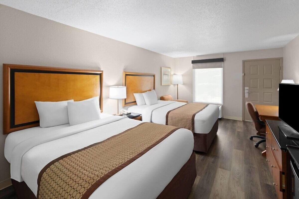 A hotel room with two beds, a desk, a chair, and a television.