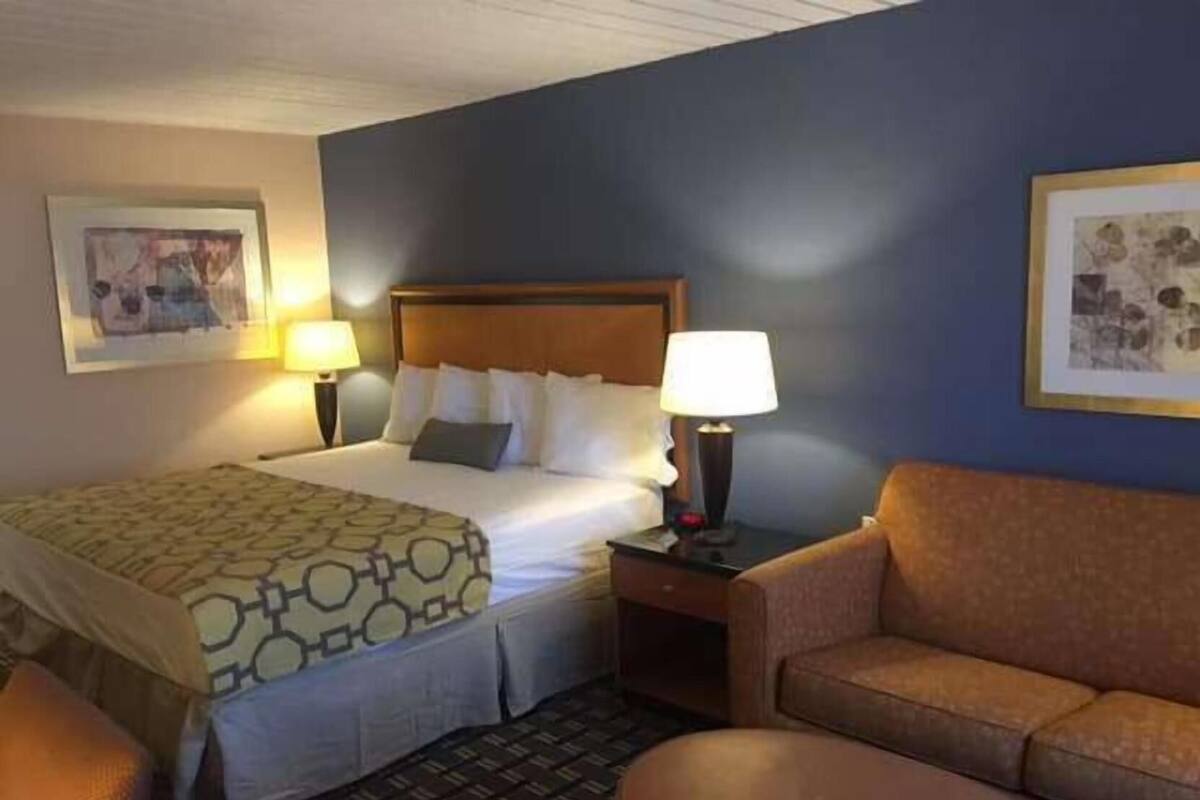 A hotel room with a bed, two bedside lamps, a brown leather sofa, a small table, and two framed pictures on the walls.