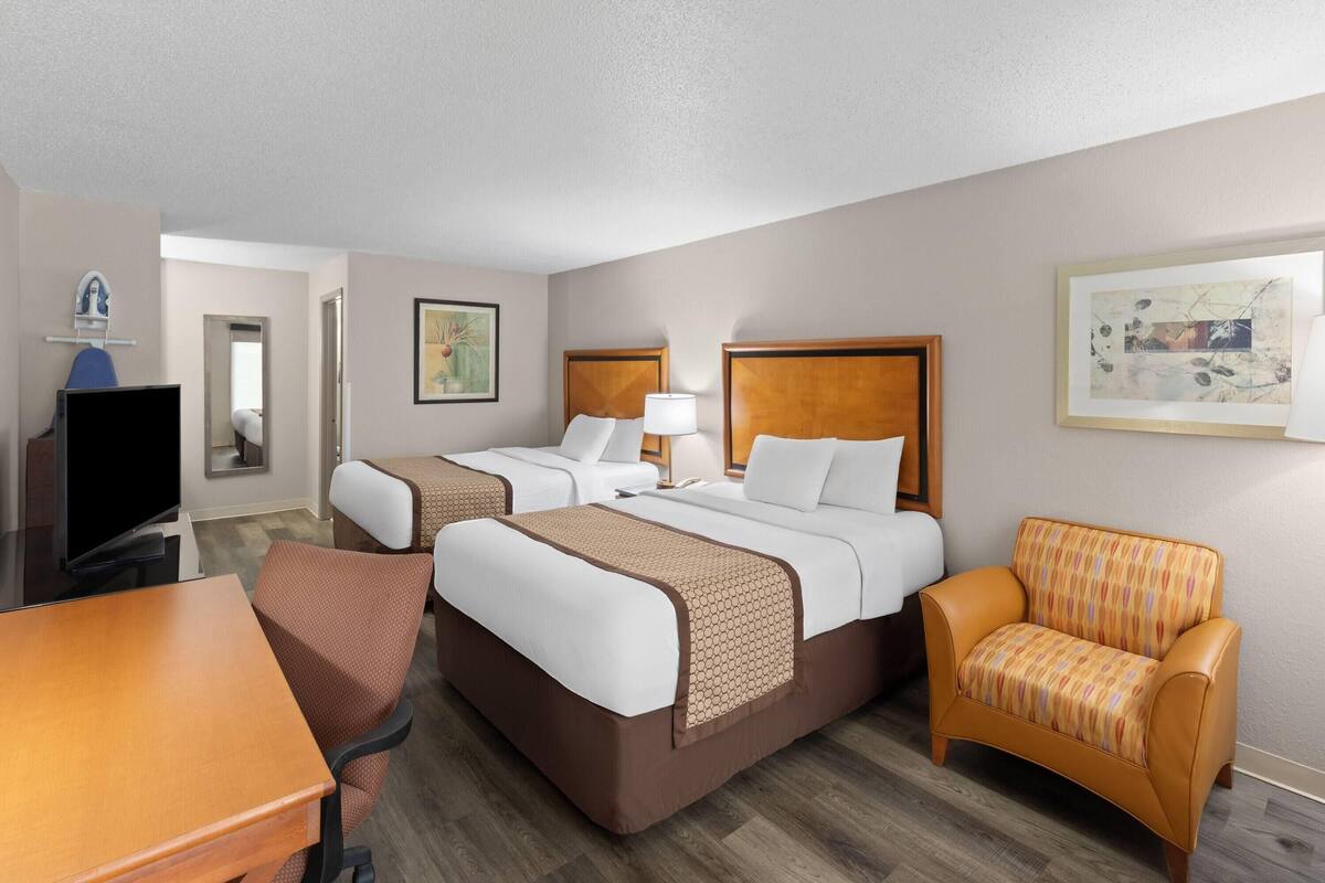 A hotel room with two beds, a TV, a desk, and a chair.