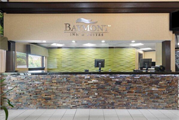 A reception area with a Baymont Inn & Suites sign, a stone wall, and a green patterned wall.