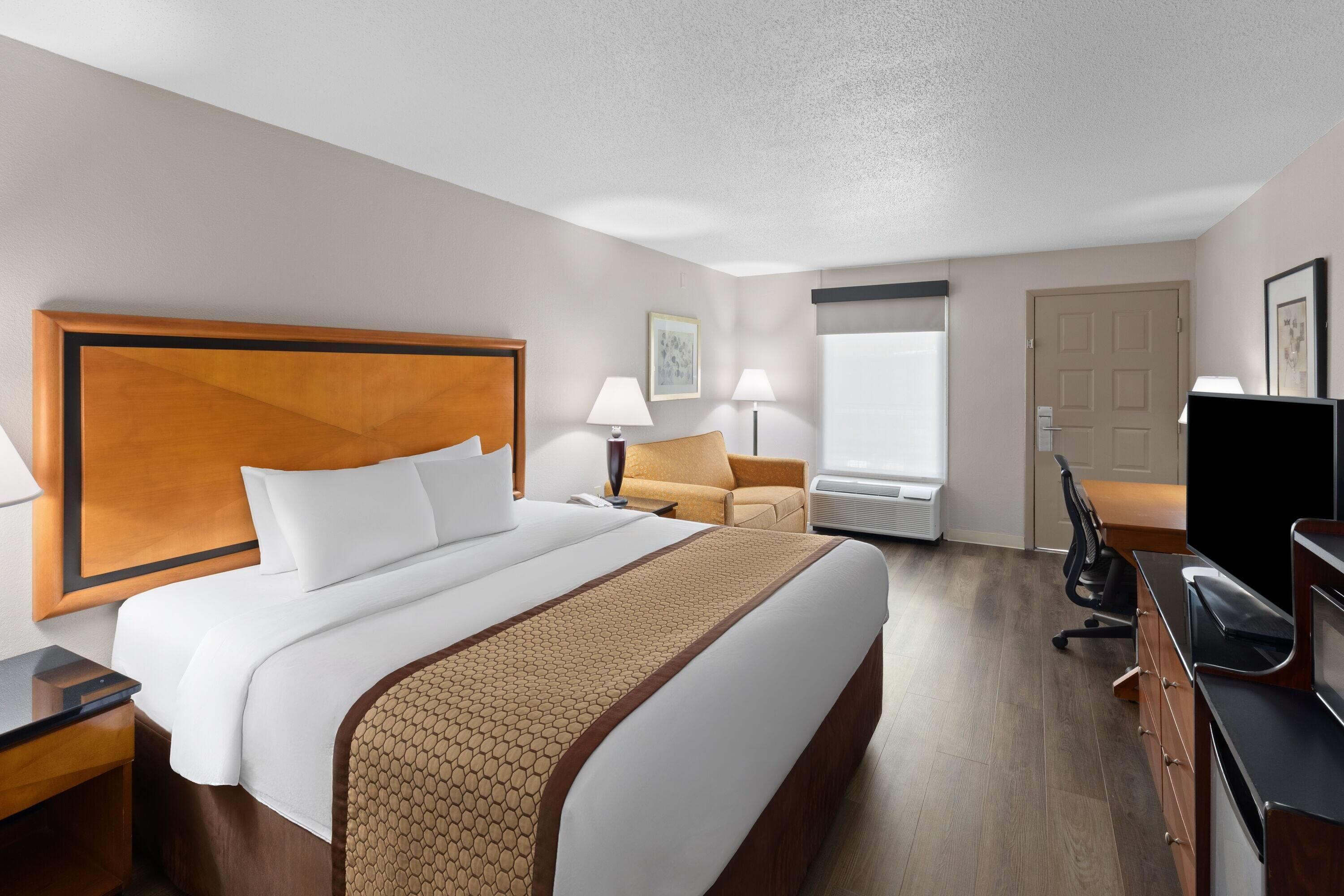 A hotel room with a large bed, a desk with a computer, a chair, a TV, and a window.