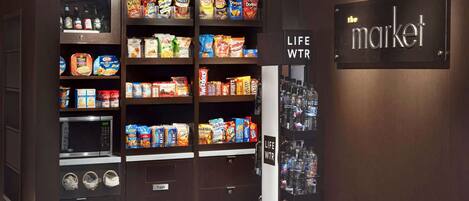 A vending machine stocked with snacks and beverages, a microwave, and a trash bin.