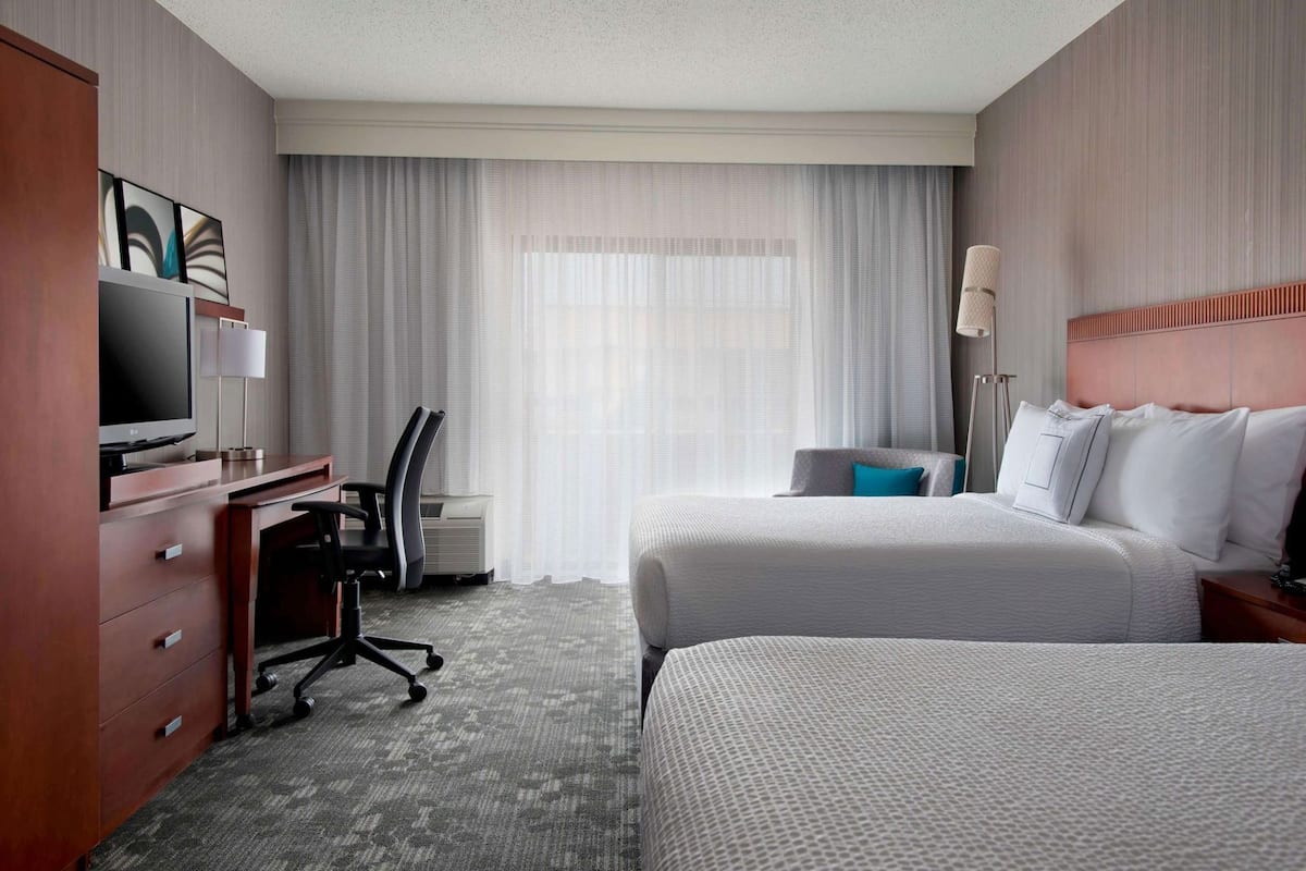 A hotel room with a bed, desk, chair, TV, and curtains.