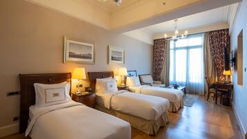 Habitación de hotel con tres camas, un candelabro y un ventanal grande con cortinas.