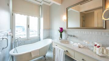 Un baño con bañera independiente, un espejo grande y una ventana con vista a edificios.