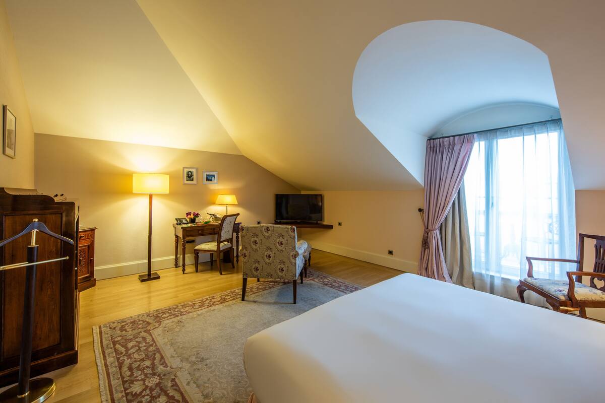 A hotel room with a large bed, a desk with a chair, a television, and a window with curtains.