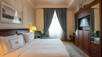A hotel room with a large bed, a desk, a chair, a wardrobe, and a television.