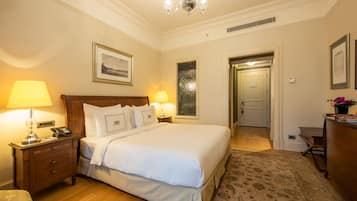 A hotel room with a large bed, two bedside lamps, a nightstand, a wooden dresser, and a chandelier.