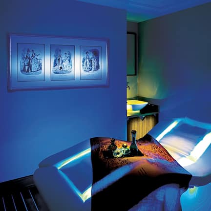 A room with a massage table, a framed picture on the wall, and a sink area.