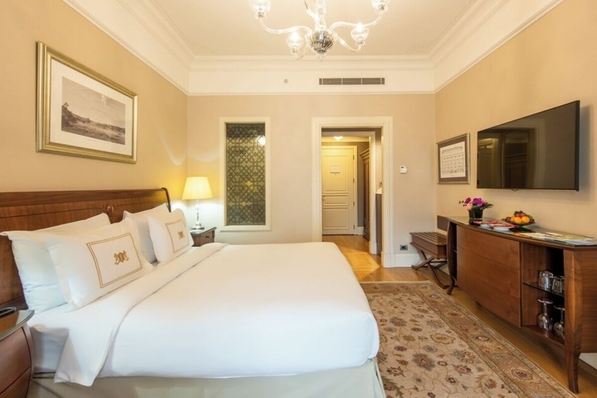 A hotel room with a large bed, a desk, a television, and a chandelier.